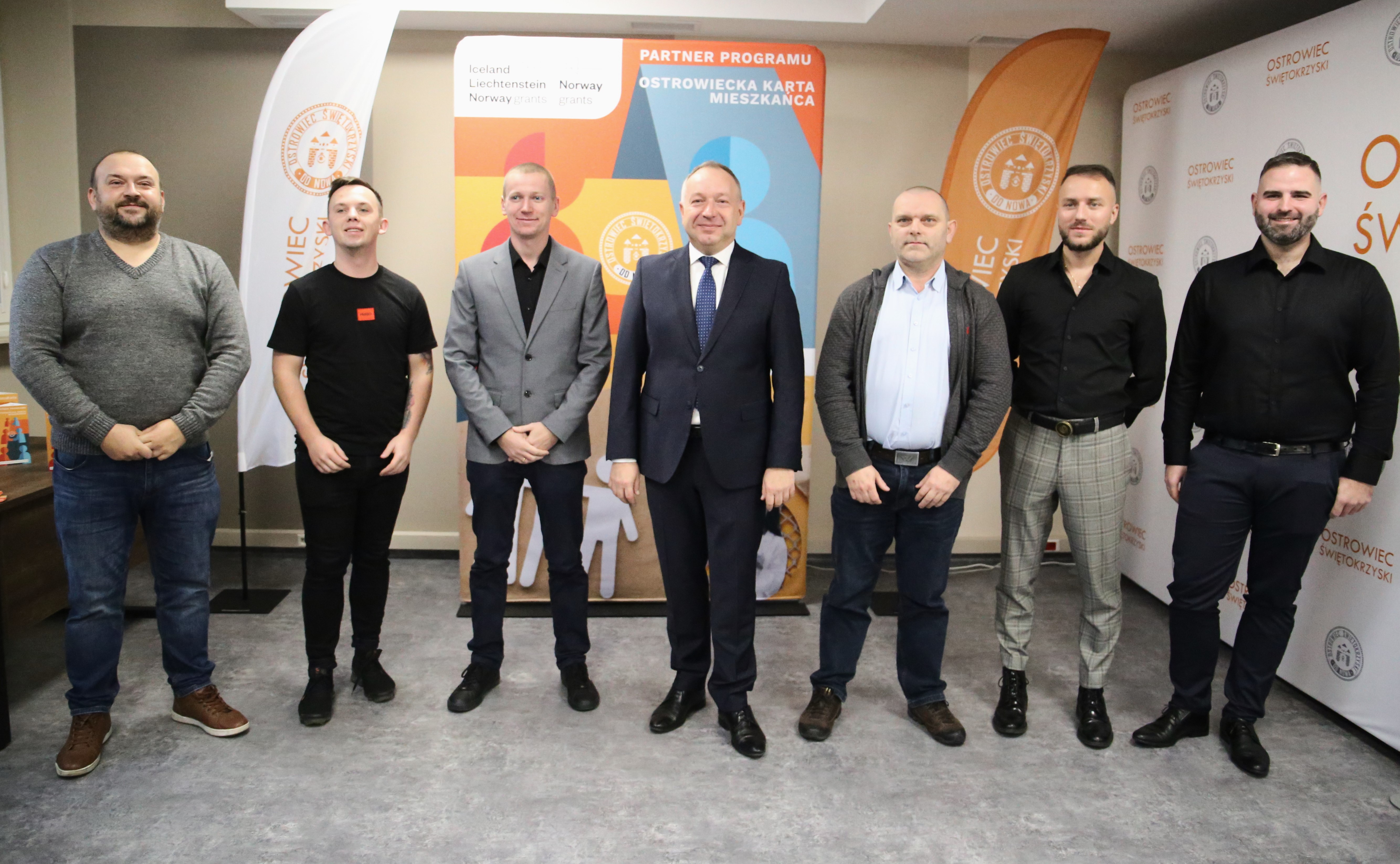 Grupa mężczyzn stoi na&nbsp;ściance promocyjnej Urzędu Miasta